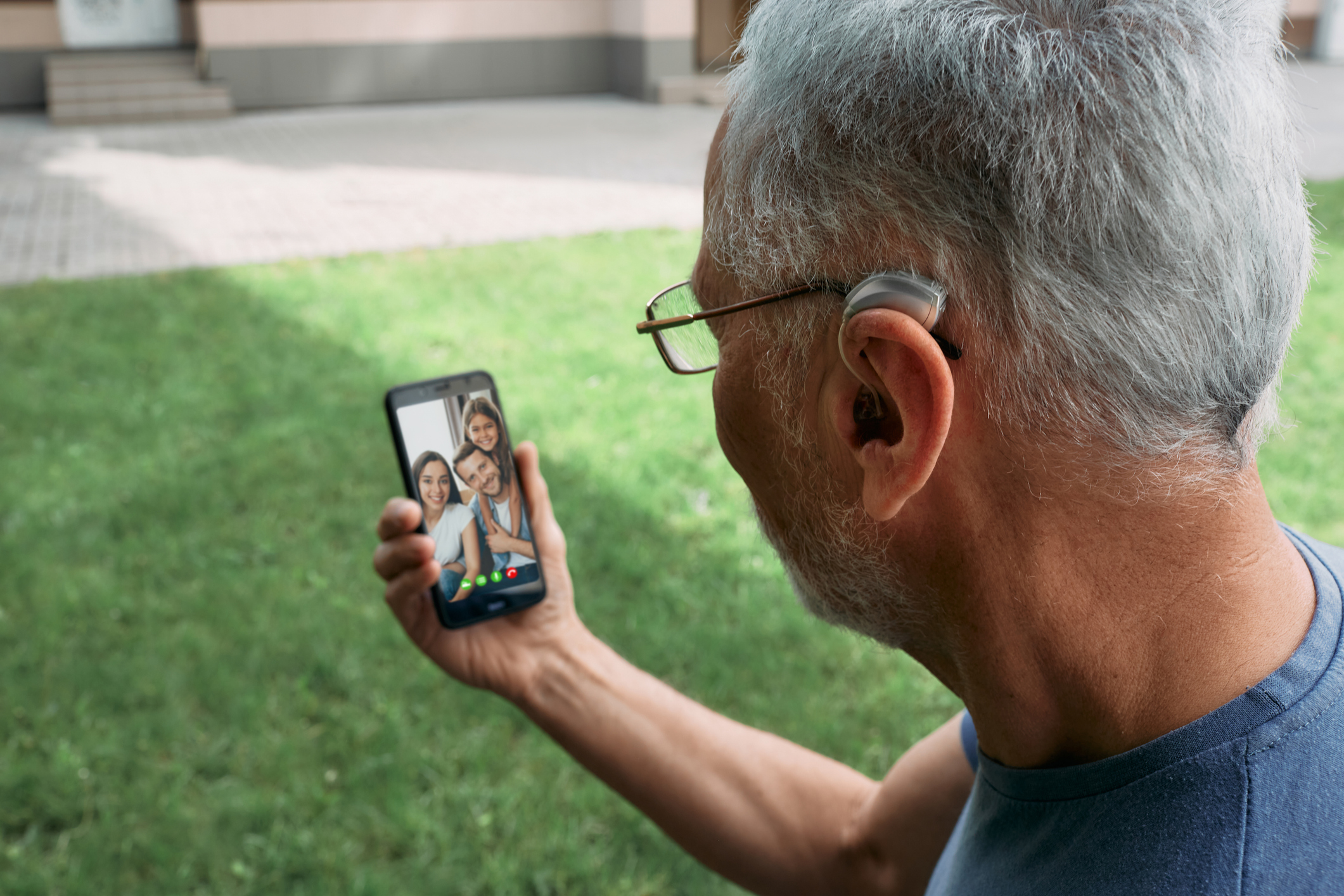 Senior man with a hearing aid behind the ear communicates with his family via video communication via a smartphone. Full human life with hearing aids