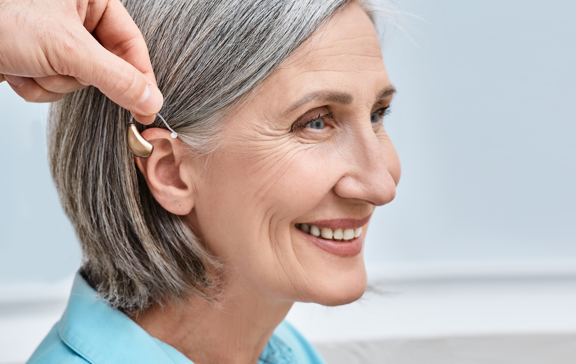 Close-up of hearing aid near senior female patient's ear at audiology clinic. Hearing solutions, hearing BTE aids
