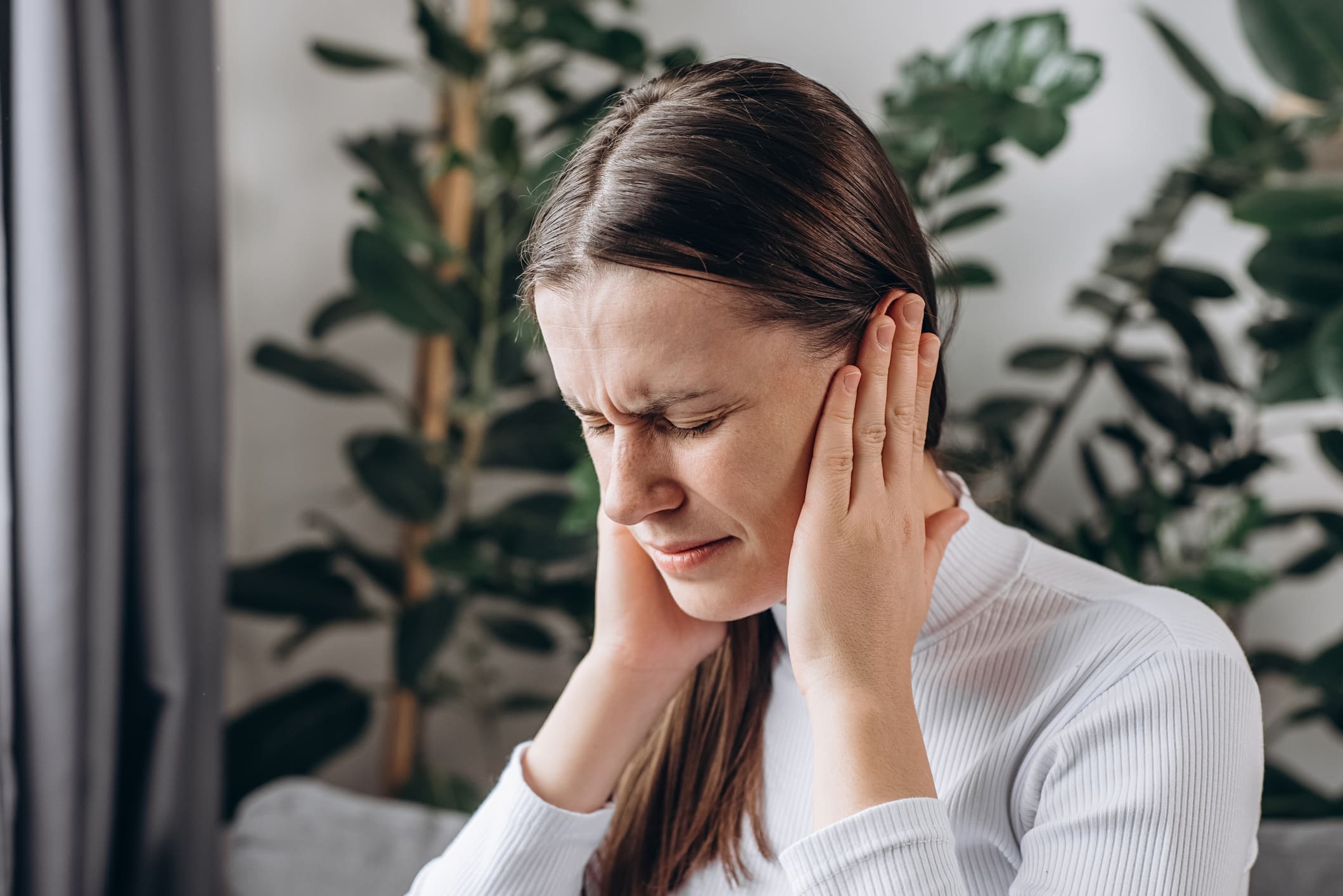 Sick young woman sit on sofa have ear pain or earache, hand touch plug ear, suffering painful otitis from loud of noisy sound, inflammation. Health care nerve deaf eardrum disease. Tinnitus concept